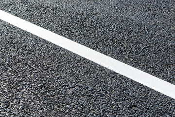 Fototapeta premium A close-up view of a solid white traffic marking line on a rough, dark asphalt pavement surface.
