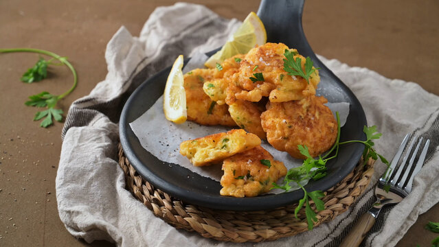 Crispy corn fritters served in a black pan with lemon wedges and fresh parsley