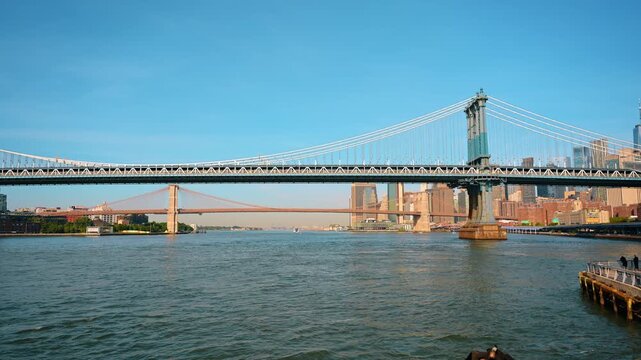 Manhattan Bridge framing Brooklyn Bridge and Lower Manhattan. Layered suspension structures cross the East River under a clear Independence Day sky.