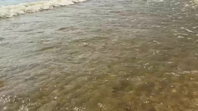 Close up video footage of gentle river waves and clear water splashing on a sandy beach. Concept of river current, freshwater, natural flow, summer shoreline, relaxing background, and eco tourism. Hig