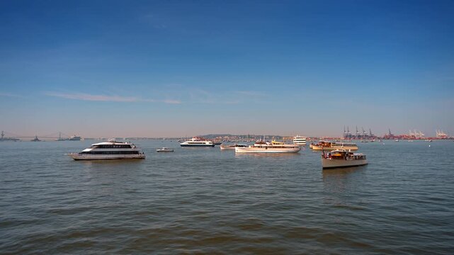 Cruise boats and yachts gathered on New York Harbor. Several commercial and private vessels float on calm water under a vast blue sky.