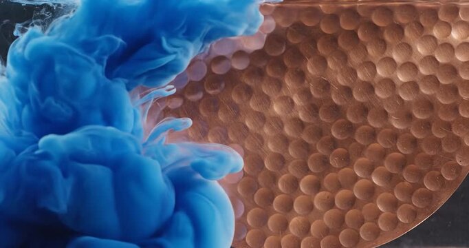Blue Ink Dropping Into Water Against A Textured Copper Surface