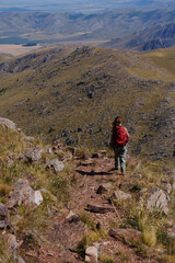 Naklejka premium female hiker hiking away from the camera with dry hills and an expansive valley in the background in the late afternoon