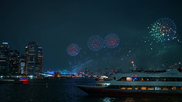 Cruise boat beneath Independence Day fireworks in New York. Passengers watch multicolored bursts above dark water and an illuminated harbor skyline.