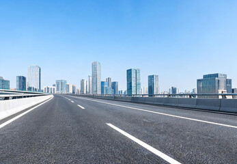 Fototapeta premium A clear, empty asphalt elevated highway stretches toward a modern city skyline under a bright blue sky.