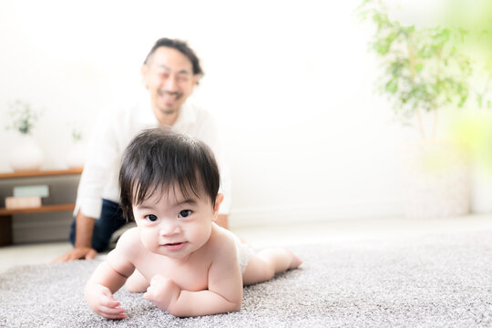 ハイハイする赤ちゃんを見守る父親 育児・子育て・成長・親子のふれあいのイクメン育休パパと赤ちゃんのイメージ