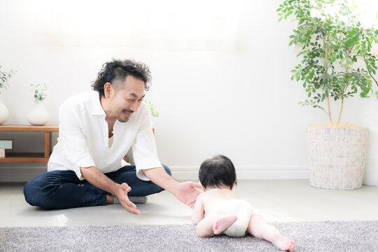 ハイハイする赤ちゃんを見守る父親 育児・子育て・成長・親子のふれあいのイクメン育休パパと赤ちゃんのイメージ
