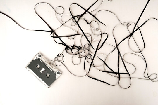 Vintage clear audio cassette tape with unspooled black magnetic film tangled across a clean white surface, perfect for retro music themes and nostalgia.
