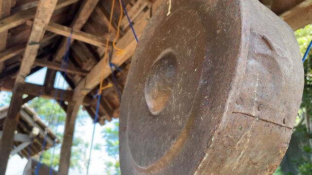A large rusty concave gong hangs from ropes within a wooden structure