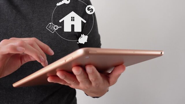 Close-up of a businesswoman interacting with her tablet, featuring an animated house icon surrounded by several money symbols. Real estate concept.