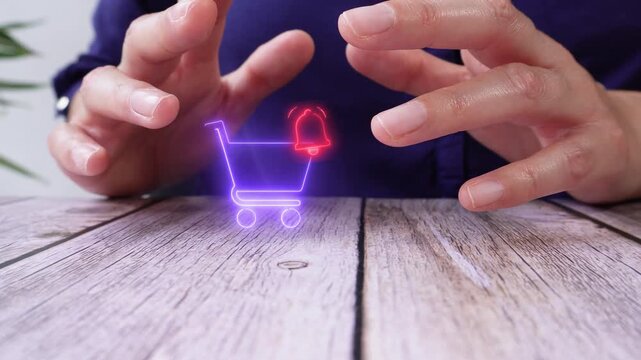 A person gestures on a wooden table. Their hands hover near a virtual shopping cart with a bell. A futuristic digital overlay appears.