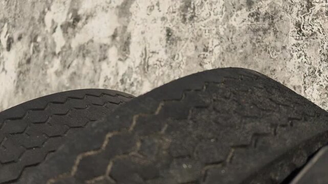 Low angle slow motion view showing the top edge profile and worn treads of black truck tires arranged against a textured wall.
