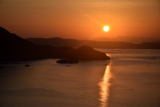 A sunrise with beautiful reddish-yellow light emerging between the hills surrounding Padar and Rinca Islands, Labuan Bajo, Indonesia.