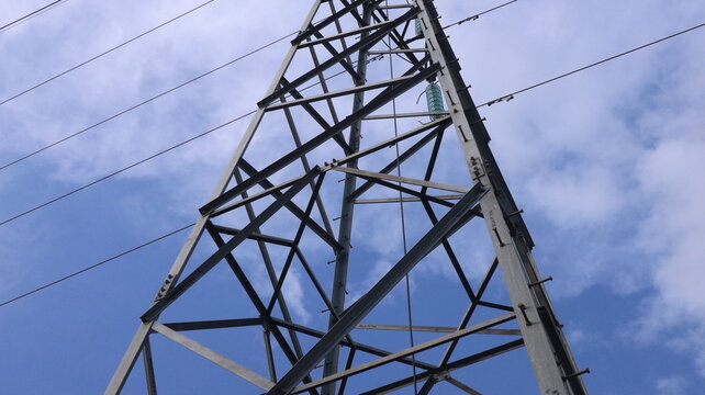 Massive steel electricity pylon tower reaching into moody sky, symbol of power, energy, industry and modern civilization dominance.