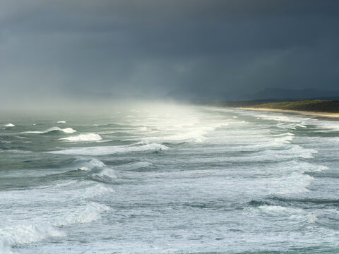 Powerful waves roll onto the coastline near Tacking Point Lighthouse in Port Macquarie, New South Wales, Australia, beneath dramatic morning storm clouds.