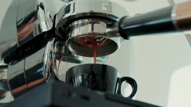 4K Pouring coffee stream from professional machine in cup. Barista man making double espresso, using filter holder. Flowing fresh ground coffee. Drinking roasted black coffee in the morning.