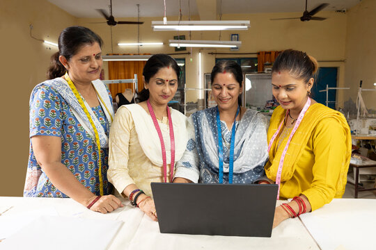 Group of skilled Indian women workers collaborating on a laptop inside a modern textile company. Female employees using digital technology for production planning, quality control and training.