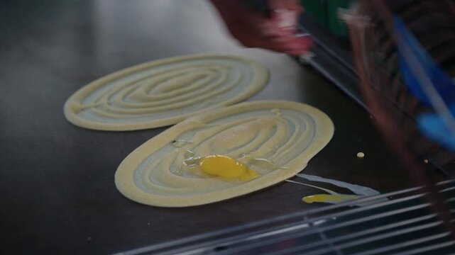 Asian street food vendor preparing thin pancake rolled crepe with sausage on hot pan.