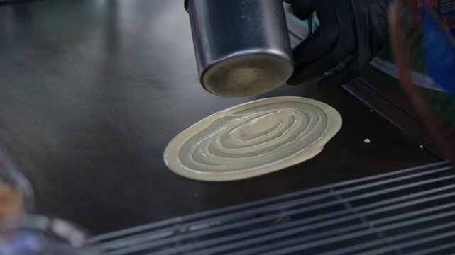 Asian street food vendor preparing thin pancake rolled crepe with sausage on hot pan.