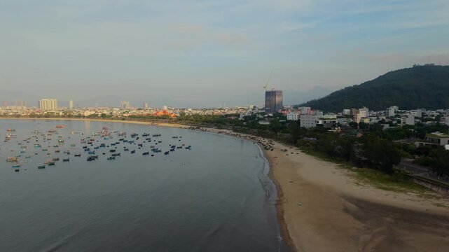 Drone aerial view of a quiet beach, fishing boats and the coastal skyline of Da Nang during a calm sunrise in Vietnam.