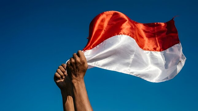 Hands holding Indonesian flag against clear blue sky.