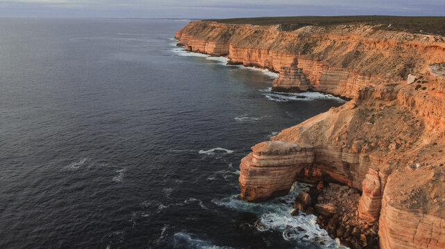 Wide angle aerial view of Island Rock and Natural Bridge coastal cliffs near Kalbarri, Western Australia. Golden glowing sandstone and vast dark ocean. Copy space. Travel, tourism