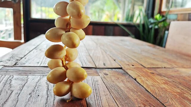 Fresh Yellow Date Palm Bunch Hanging Vertically Over Wooden Table.