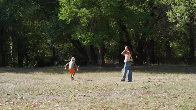 A cheerful mother and her playful son enjoy a game of badminton in a sunny park clearing. They feel completely happy and energized during this active family day.