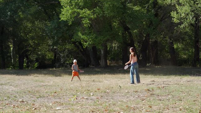 A cheerful mother and her playful son enjoy a game of badminton in a sunny park clearing. They feel completely happy and energized during this active family day.