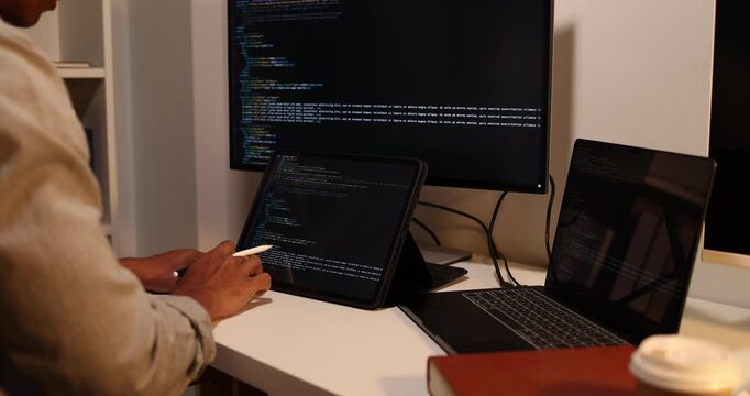 Software developer writing, reviewing and debugging source code across multiple screens using tablet and computer in modern workspace for software engineering, programming and application development.
