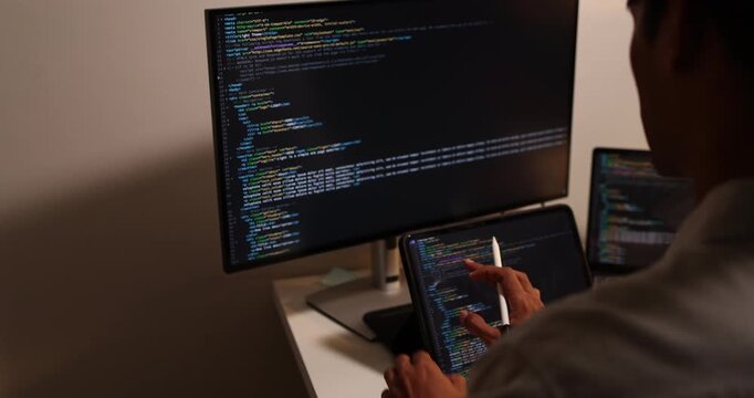 Software developer writing, reviewing and debugging source code across multiple screens using tablet and computer in modern workspace for software engineering, programming and application development.
