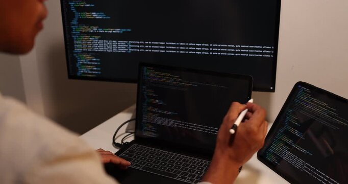 Software developer writing, reviewing and debugging source code across multiple screens using tablet and computer in modern workspace for software engineering, programming and application development.