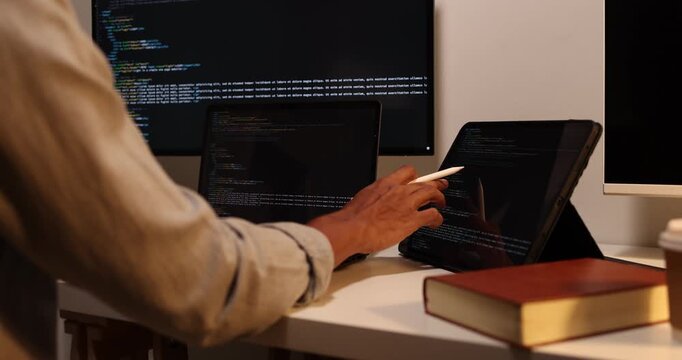 Software developer writing, reviewing and debugging source code across multiple screens using tablet and computer in modern workspace for software engineering, programming and application development.