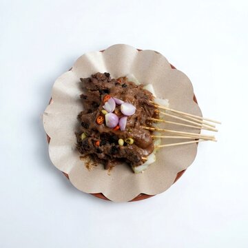 Sate Ayam with Bumbu Kacang, Lontong, and Red Shallots Served on Brown Paper, Isolated.