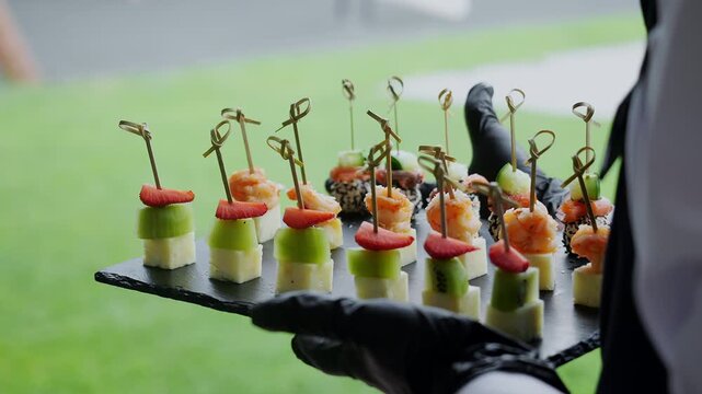 Professional waiter serving assorted gourmet canapes on a catering tray during a wedding, corporate event or reception. Elegant finger food for buffet and hospitality service.