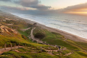 Obraz premium People hiking on a cliffside trail at Fort Funston in Daly City, California, enjoying a scenic walk down to the beach at sunset.