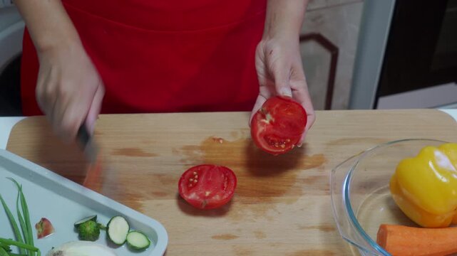 Tomato being cut with tongs, in kitchen counter, with tomato, tongs, cutting board, plate of vegetables, from a overhead perspective, with red, green accents, and focused mood, nearby objects.