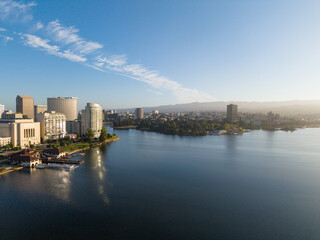 Fototapeta premium Urban skyline of Oakland California surrounding Lake Merritt, featuring downtown buildings, waterfront structures, and distant hills under a clear sky