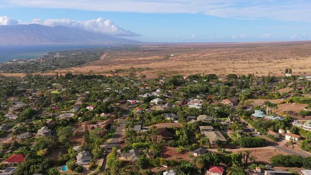 4K 60fps drone aerial video pulling back over the Maui Meadows neighborhood near Wailea. An overhead perspective shows upscale homes, tropical landscaping, and the distant Hawaiian coastline.