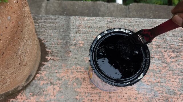 Hand Scraping Paint Brush on Edge of Black Paint Can