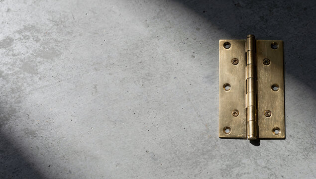 a brass door hinge screwed onto a grey concrete surface
