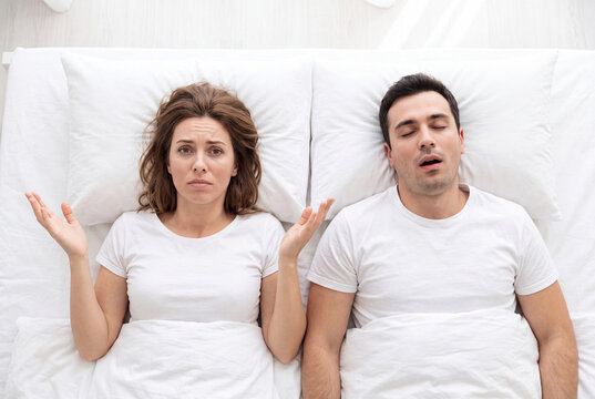 Frustrated woman lying in bed next to her snoring husband