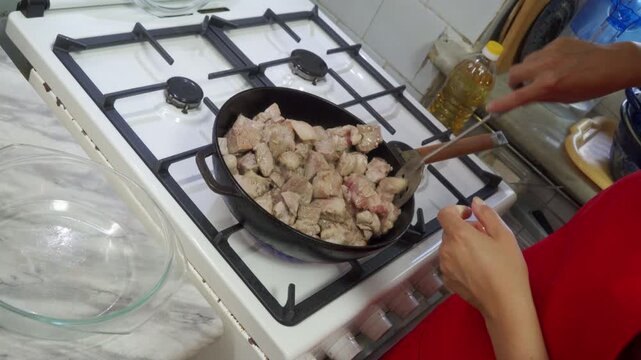 Cooking frying meat, in kitchen stove, with frying pan, gas stove, spatula, glass bowl, from a first-person perspective perspective, with red, black accents, and neutral mood, nearby objects.