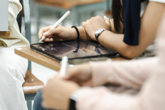Hands draw on tablet with stylus. Focus is on creative task at wooden desk. User wears watch and bracelet. Soft lighting highlights concentration. Ideal for education or tech learning scenes