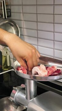 Male hand placing pieces of raw meat into electric meat grinder while preparing homemade minced meat in home kitchen, 4K.