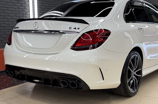 Rear three-quarter view of a white Mercedes-AMG C 43 luxury sports sedan parked indoors. High performance German automobile with carbon fiber spoiler, quad exhaust tips, and alloy wheels.
