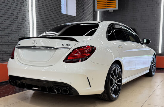 Rear three-quarter view of a white Mercedes-AMG C 43 luxury sports sedan parked indoors. High performance German automobile with carbon fiber spoiler, quad exhaust tips, and alloy wheels.