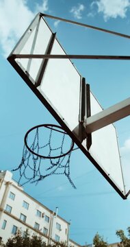 Basketball Entering Outdoor Metal Chain Hoop Against Blue Sky