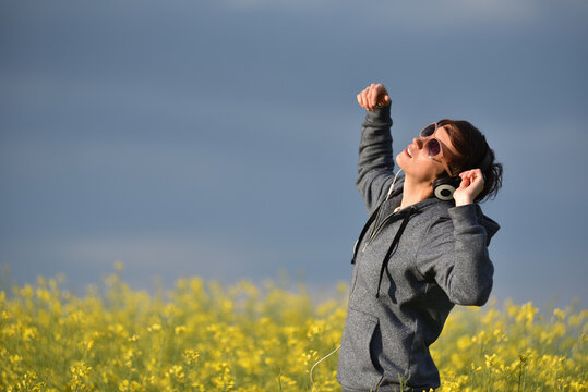Woman with headphones listening to music in a yellow canola flower field