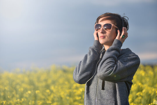 Woman with headphones listening to music in a yellow canola flower field
